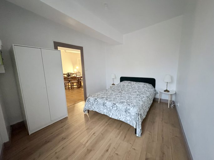Chambre lumineuse avec lit, armoire et table de chevet, sol en bois.