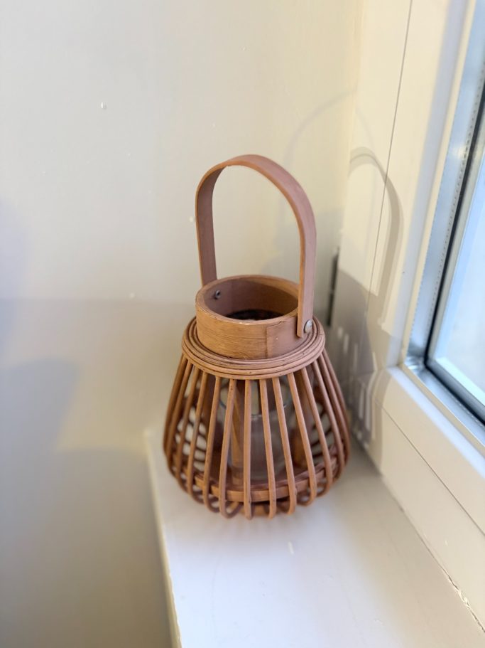 Panier en osier, de couleur marron, avec une anse, posé près d'une fenêtre.